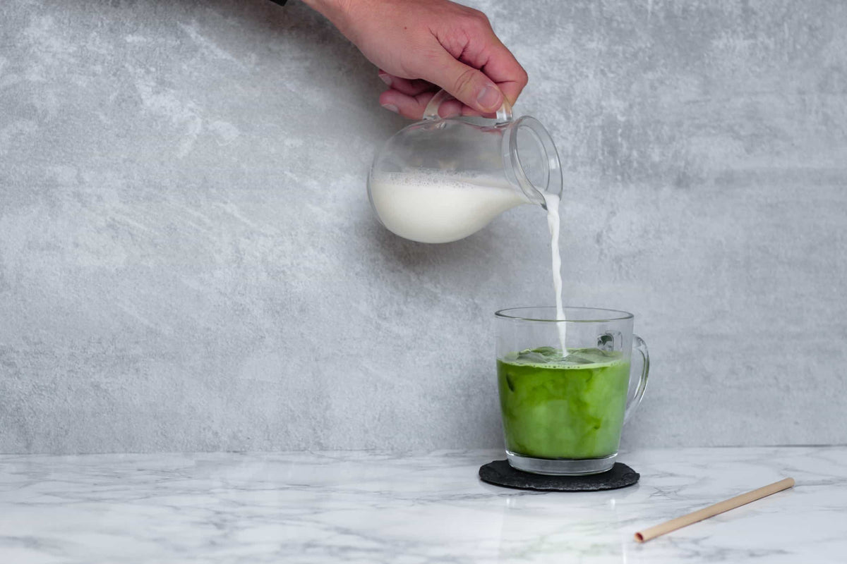 Milch wird in ein Glas mit kaltem Matcha Latte gegossen