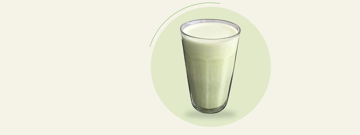 Verre de smoothie au matcha, à la banane, à l’avoine et à la vanille, sur fond crème et vert.