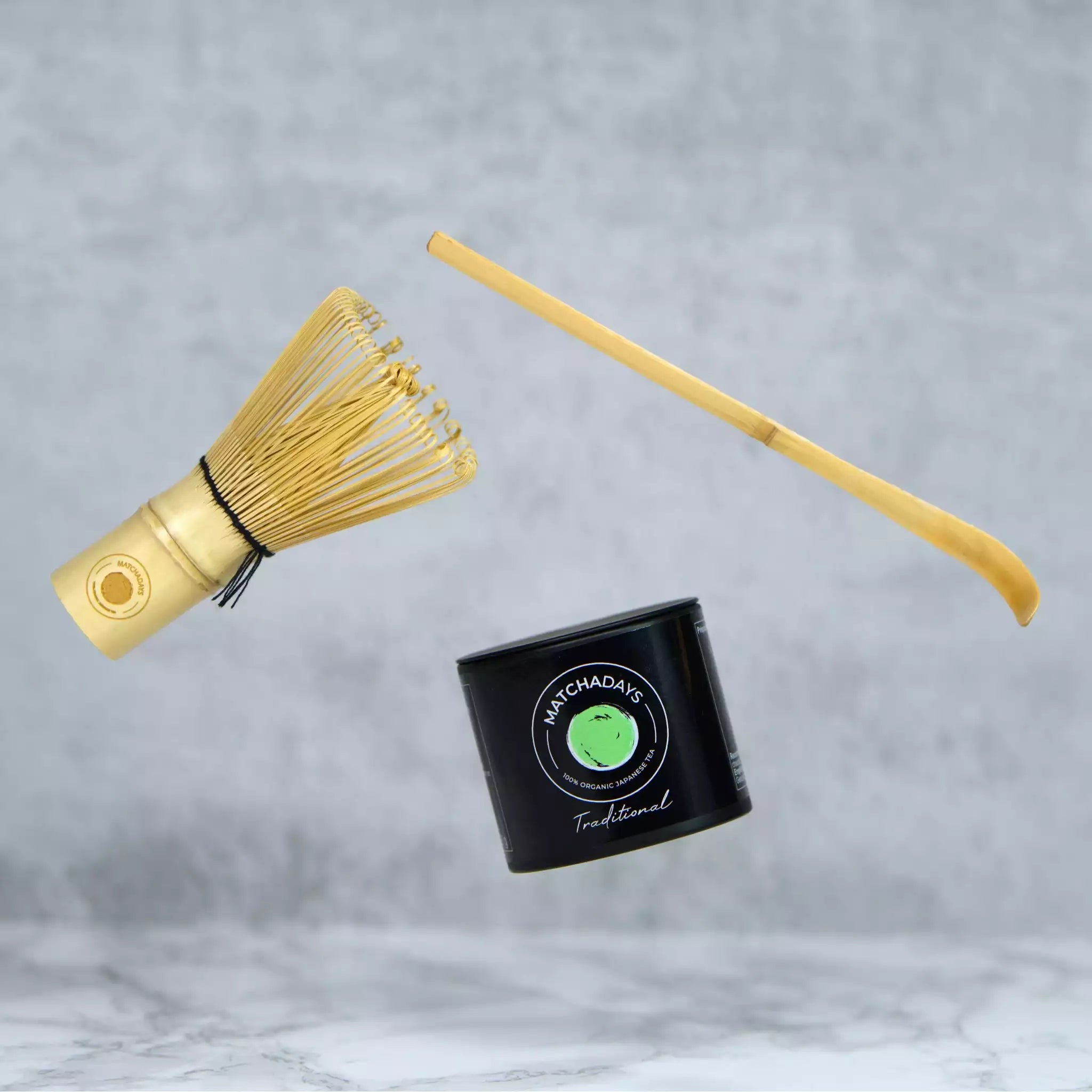 Photo d'une boîte de matcha traditional de MatchaDays avec à côté une cuillière (chashaku) et un fouet à matcha (chasen).
