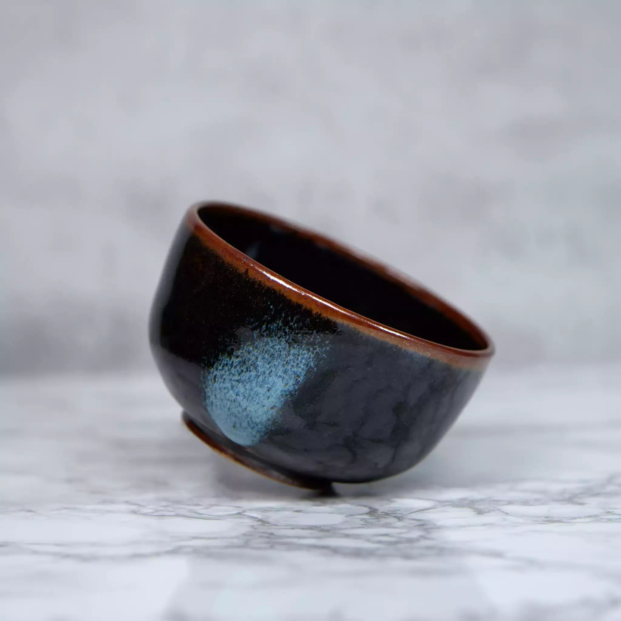 Bol pour thé matcha en céramique fait main appelé chawan de couleur noir et brun avec des tâches bleues